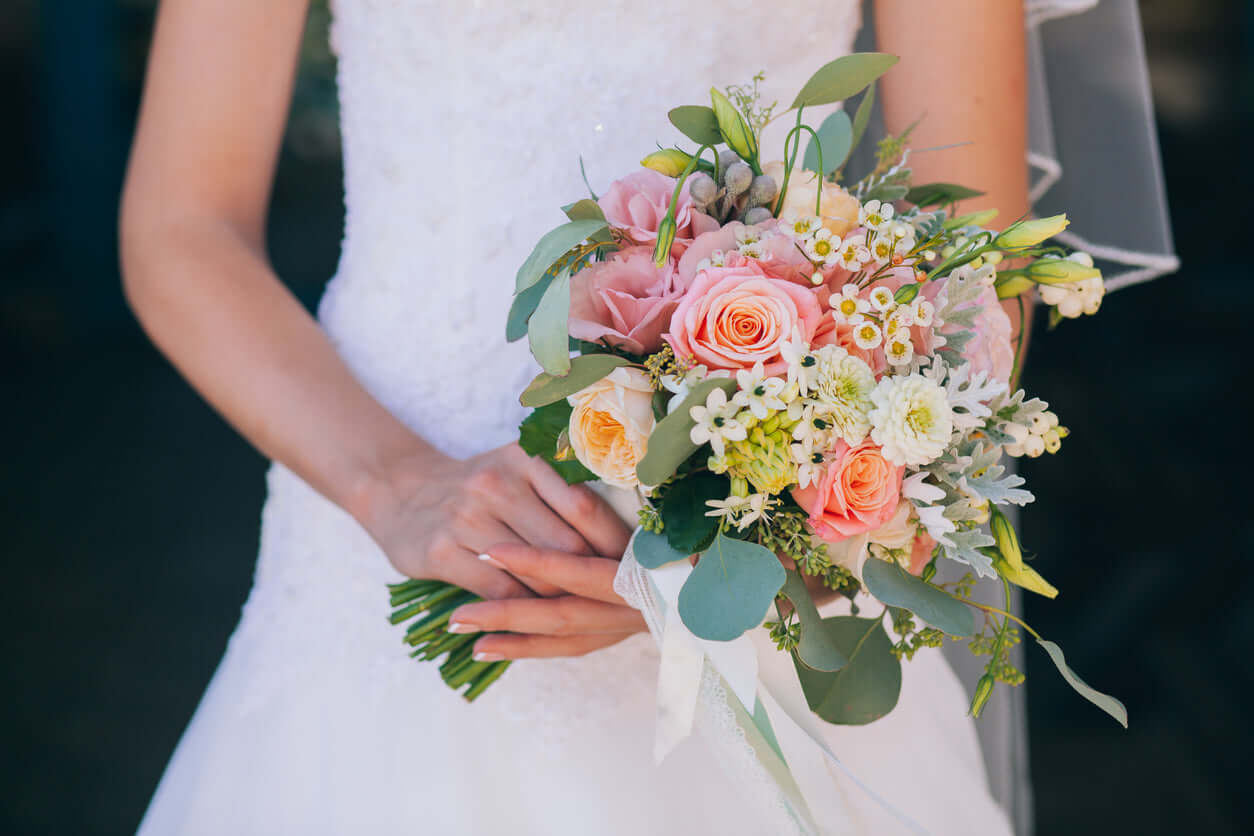 Brautstrauß "Laurentina" mit Pfirsich-, Rosa- und Weißtönen, präsentiert von einer Braut in einem weißen Kleid.