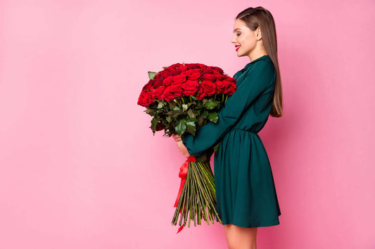 Frau mit einem großen Bukett aus roten Rosen 80cm lang vor rosa Hintergrund.